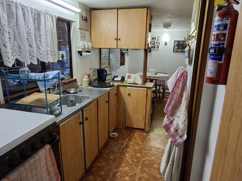 A compact, dated kitchen featuring laminate cabinetry, a stainless steel sink, and a freestanding stove, offering potential for a modern renovation.