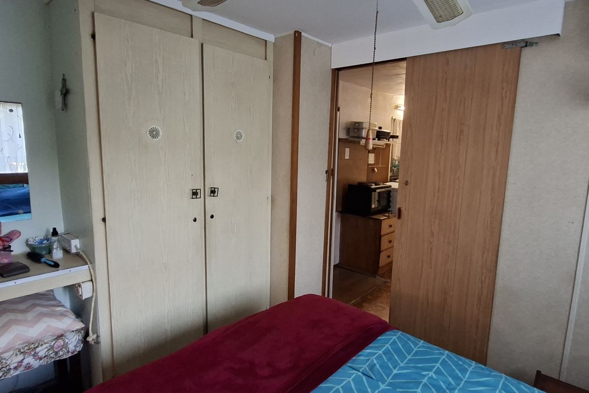 A bedroom featuring built-in wardrobes, a vanity area, and a sliding door leading to an adjacent room, with dated finishes throughout.