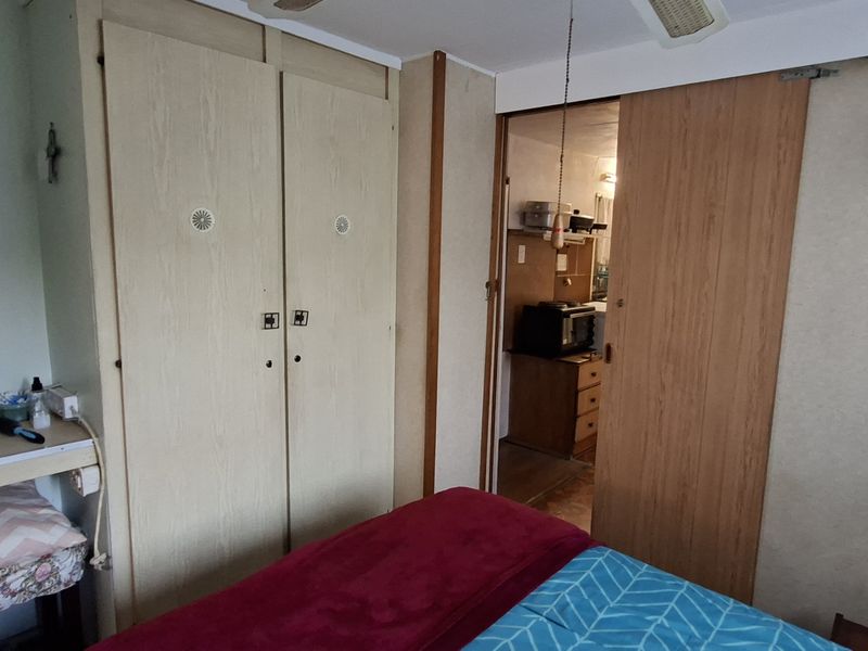 A bedroom featuring built-in wardrobes, a vanity area, and a sliding door leading to an adjacent room, with dated finishes throughout.