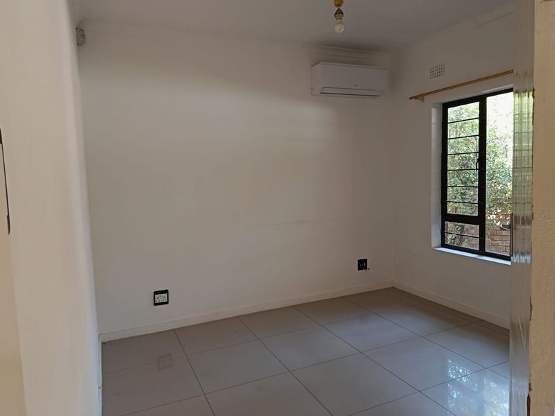 An empty bedroom featuring tiled flooring, a wall-mounted split-system air conditioner, and a window with security bars.
