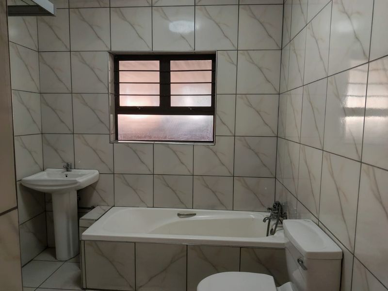 A functional bathroom featuring a pedestal washbasin, built-in bathtub, and toilet, finished with neutral wall and floor tiling.