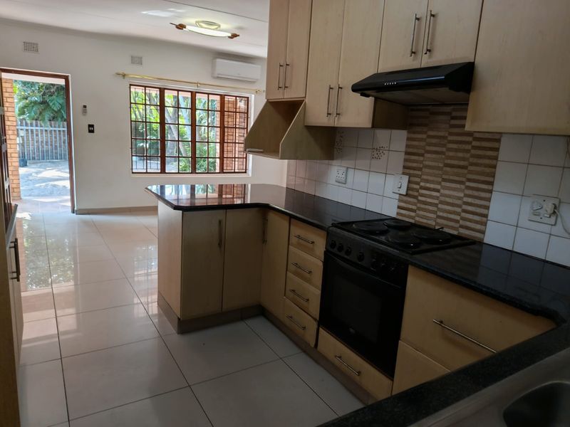 Open-plan kitchen featuring light wood cabinetry, granite countertops, and integrated appliances, flowing into a bright living area with direct outdoor access.