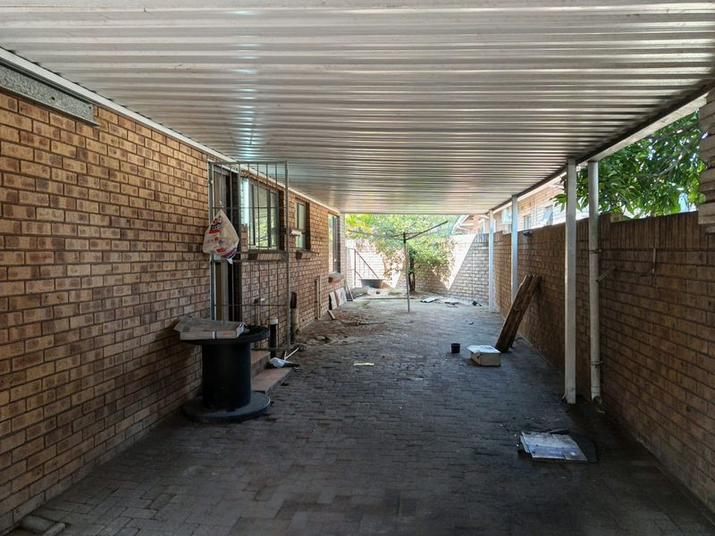 A covered outdoor patio area featuring brick walls, paved flooring, and a corrugated metal roof, offering a functional space for outdoor use.