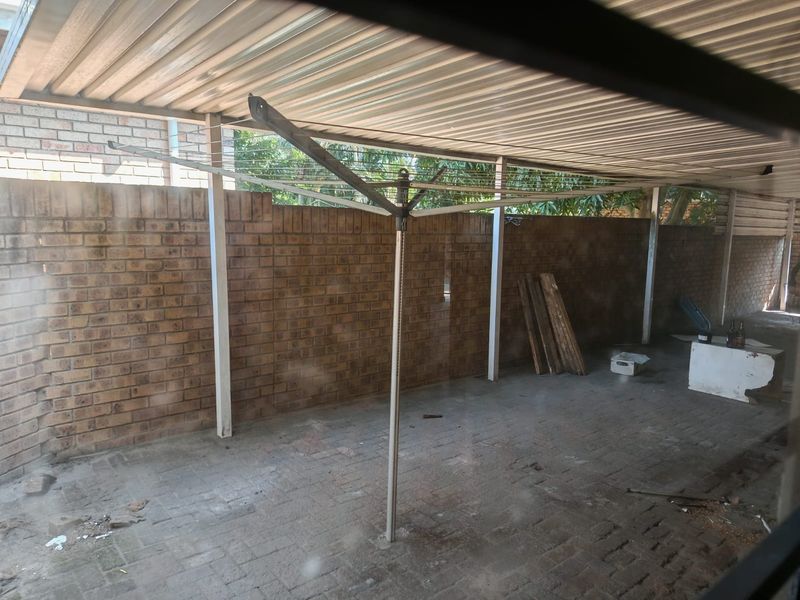 A covered outdoor patio area featuring a corrugated metal roof, brick boundary walls, and paved flooring, suitable for a functional utility or entertainment space.
