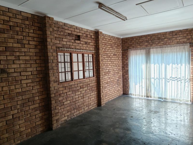 An empty living area featuring exposed brick walls, concrete flooring, and a timber-framed window, offering a blank canvas for renovation.