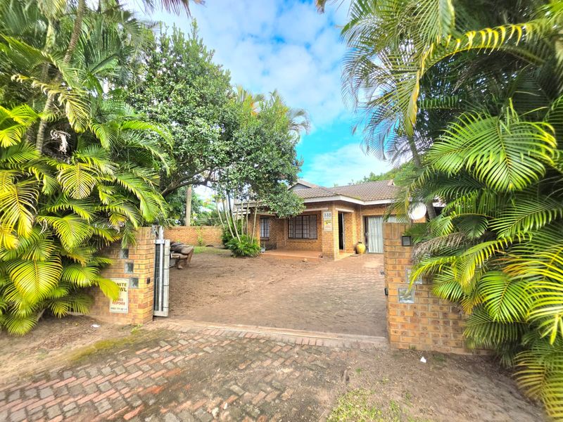 Front view of a single-story house featuring a brick facade, tiled roof, and a gated entrance with a paved driveway and established garden.