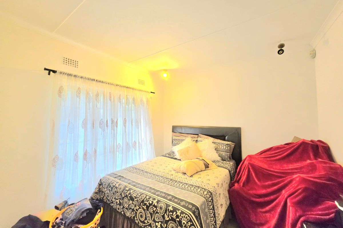 A standard bedroom featuring a window with curtain rod and ventilation grille, providing a functional space for rest.