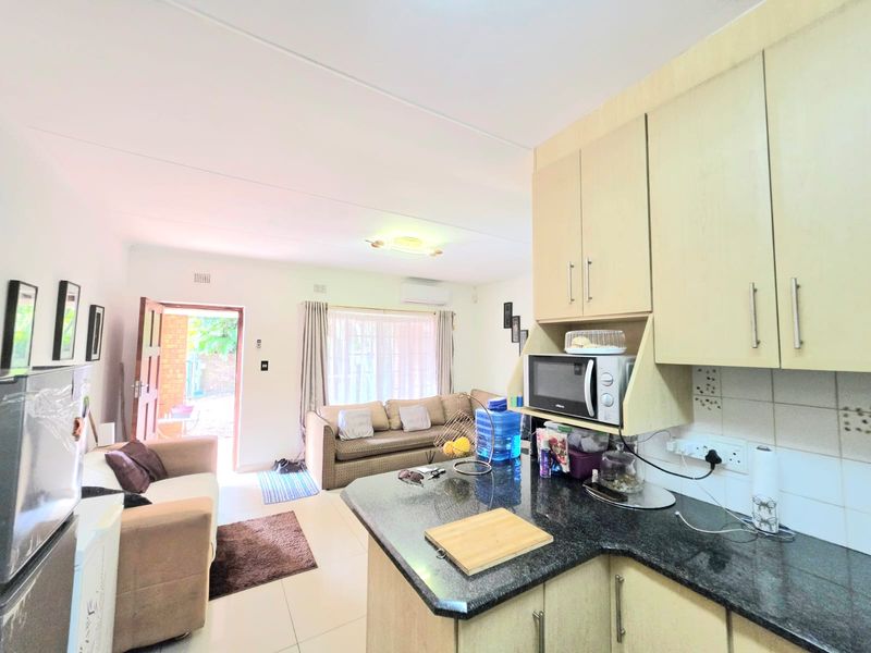 Open-plan living area featuring a functional kitchen with granite countertops and built-in cabinetry, seamlessly flowing into the adjacent lounge space with direct outdoor access.