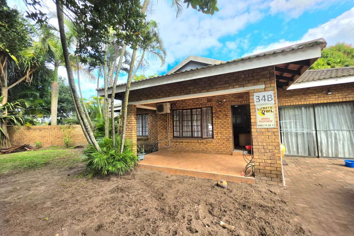 A rear view of a face brick house featuring a covered tiled patio, sliding glass doors, and an established garden area.