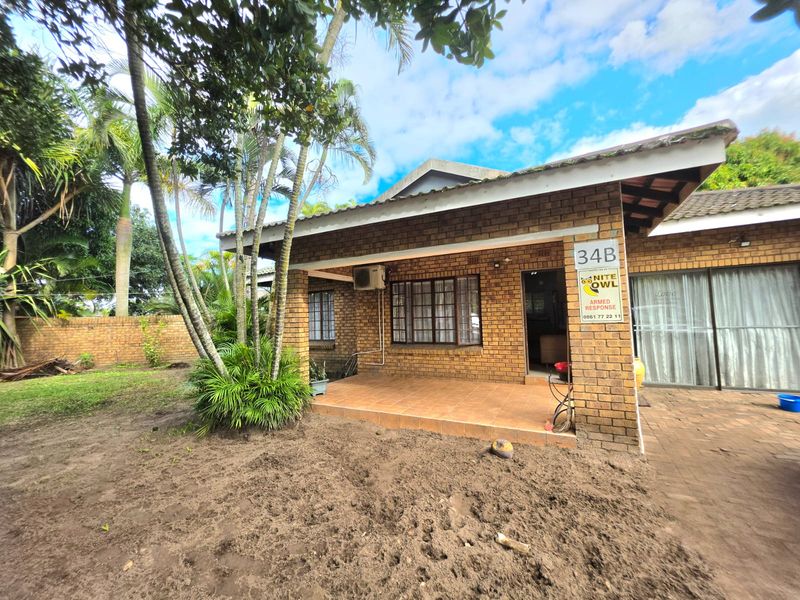 A rear view of a face brick house featuring a covered tiled patio, sliding glass doors, and an established garden area.