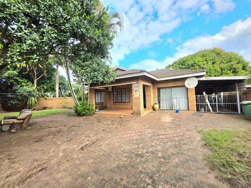 Front view of a face brick house featuring a paved driveway, covered patio, and established garden area.