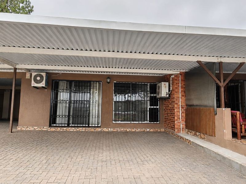 A functional front exterior featuring a large covered carport, paved driveway, and secure access points with integrated air conditioning units.