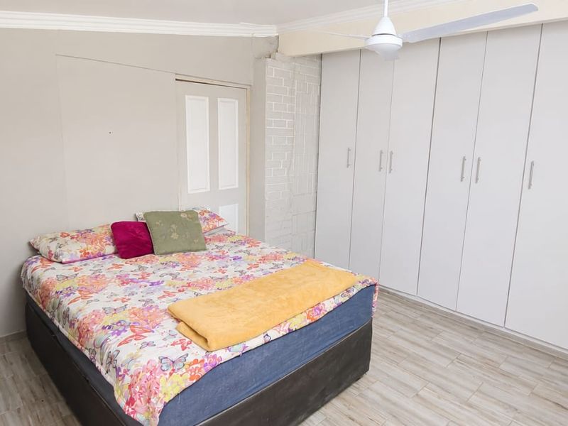 A bedroom featuring built-in cupboards, a ceiling fan, air conditioning, and laminate flooring.