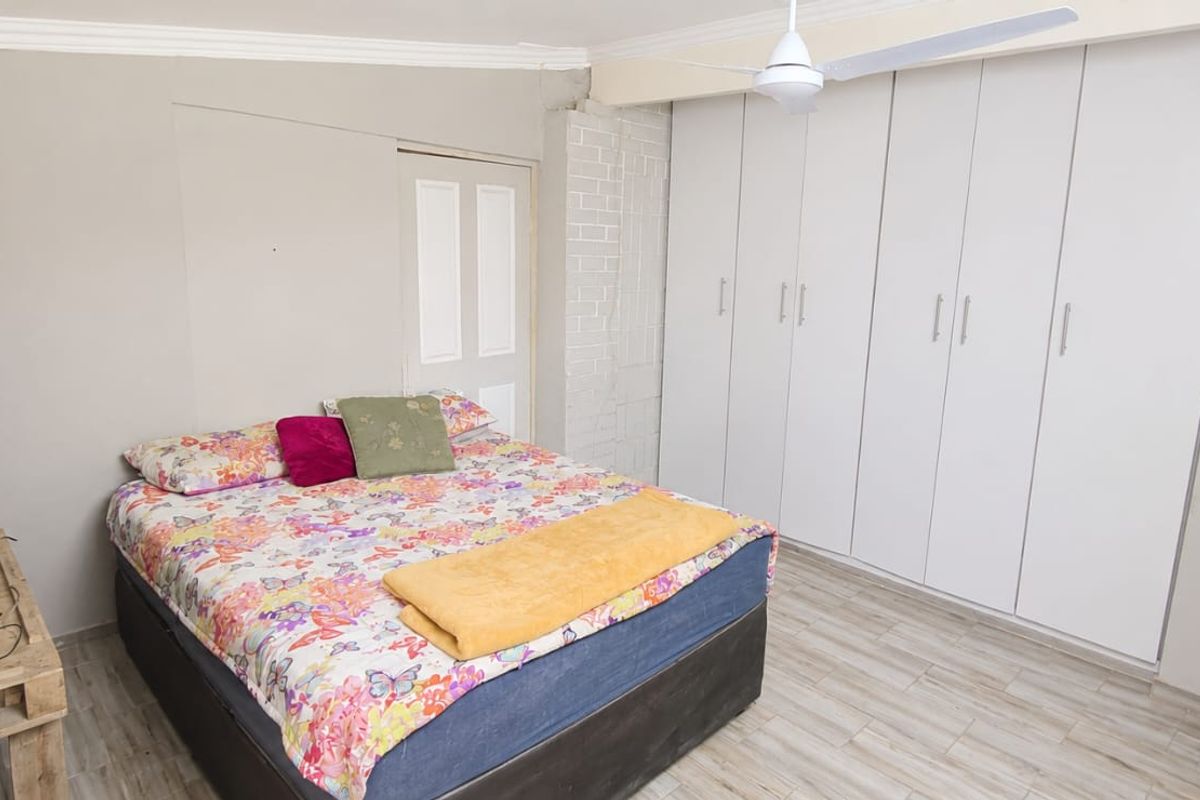 A bedroom featuring built-in cupboards, a ceiling fan, air conditioning, and laminate flooring.