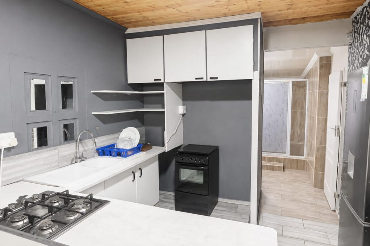 Compact kitchen featuring built-in cabinetry, a gas hob, and a freestanding oven, with direct access to an adjacent tiled area.