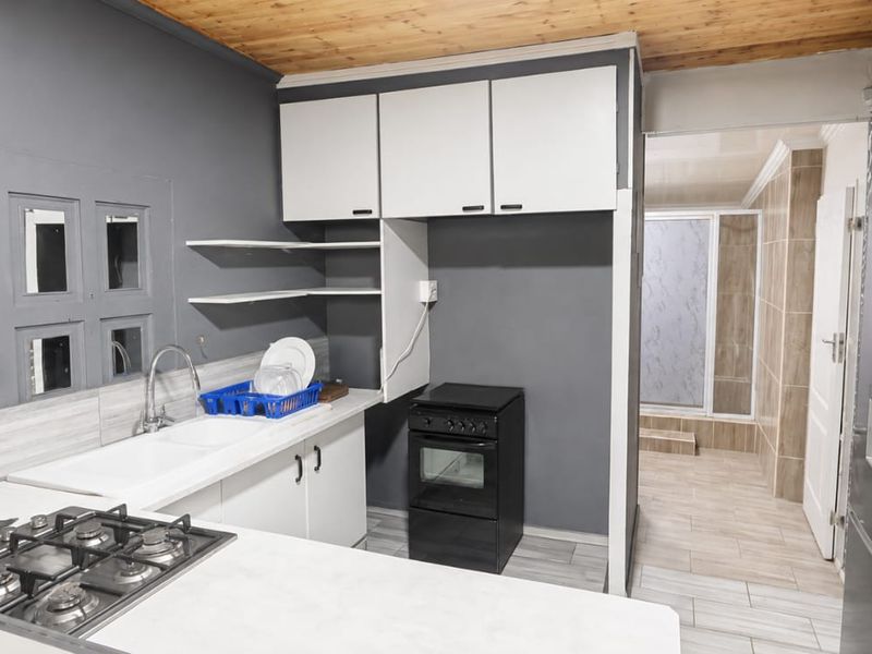 Compact kitchen featuring built-in cabinetry, a gas hob, and a freestanding oven, with direct access to an adjacent tiled area.