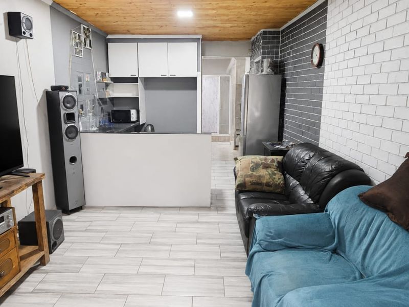 Open-plan living area featuring a kitchen with breakfast counter, exposed timber ceiling, and a textured brick feature wall with modern tiled flooring.