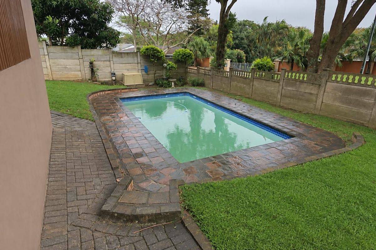 A private outdoor swimming pool area featuring a paved surround, established lawn, and secure precast concrete boundary walling.