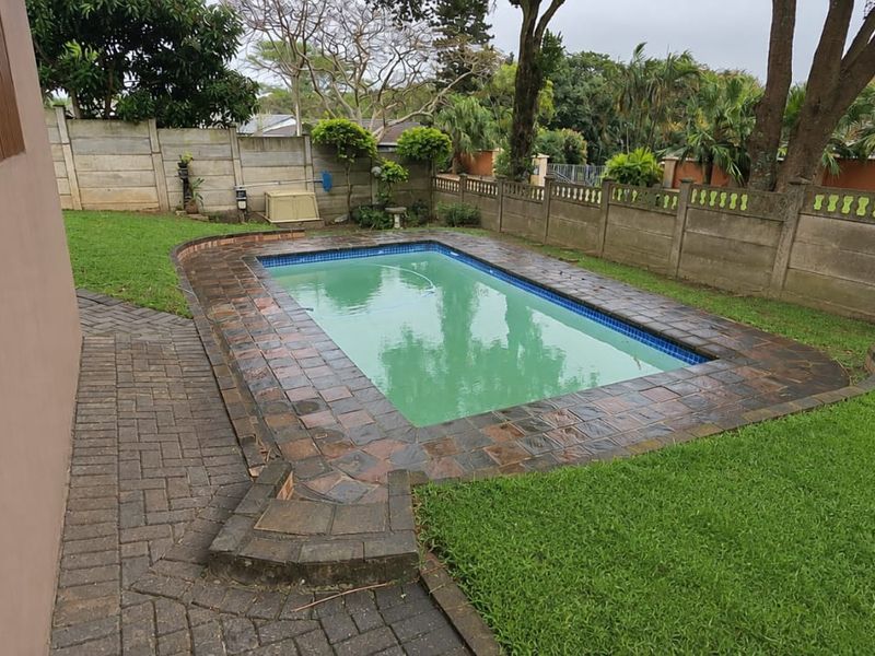 A private outdoor swimming pool area featuring a paved surround, established lawn, and secure precast concrete boundary walling.