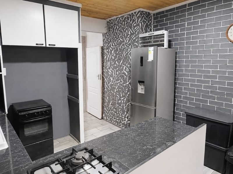 Open-plan kitchen featuring dark stone countertops, built-in cabinetry, gas hob, and an exposed brick feature wall, seamlessly connecting to the living area.