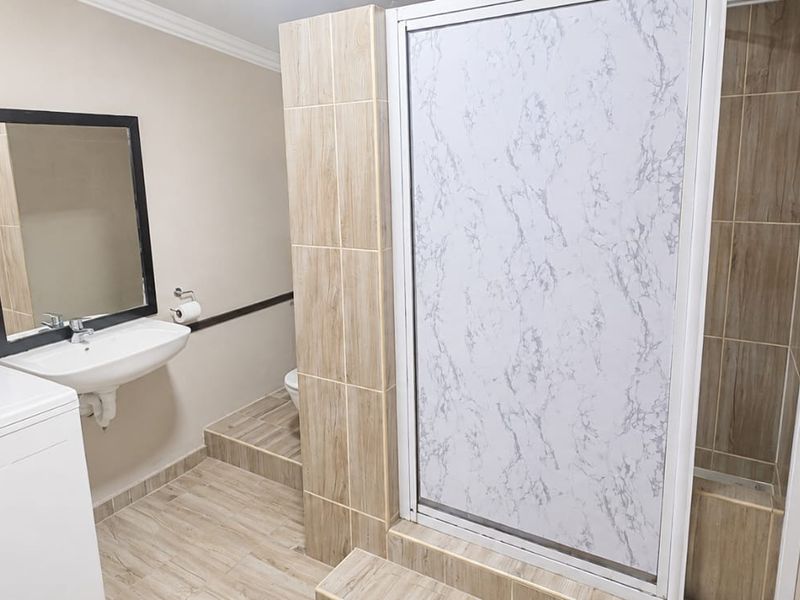 A functional bathroom featuring a shower enclosure, wall-mounted basin, and neutral tiled finishes throughout.