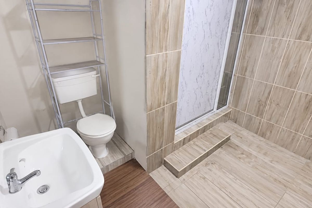 A functional bathroom featuring a shower enclosure, toilet, and washbasin with wood-look tiled flooring and wall accents.