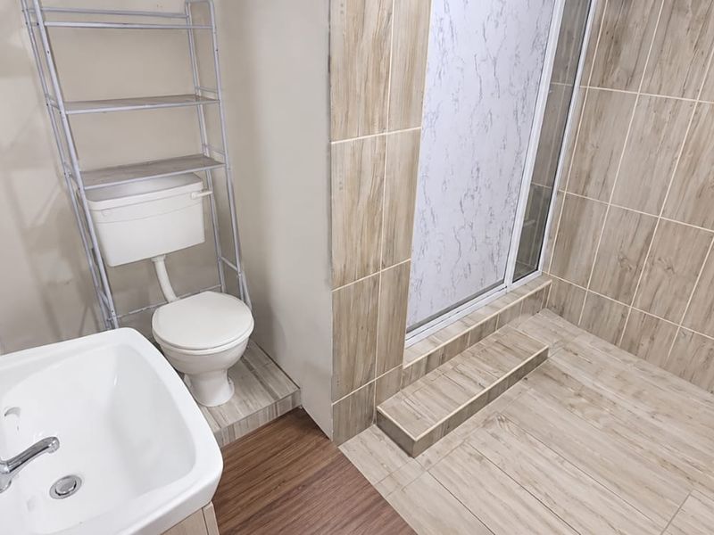 A functional bathroom featuring a shower enclosure, toilet, and washbasin with wood-look tiled flooring and wall accents.