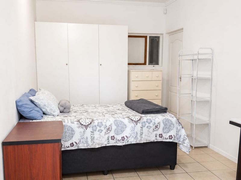 A functional bedroom featuring neutral tiled flooring, white walls, and a built-in wardrobe providing ample storage space.