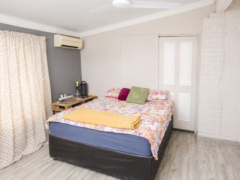 A bedroom featuring built-in cupboards, an exposed brick accent wall, laminate flooring, and an installed air conditioning unit.