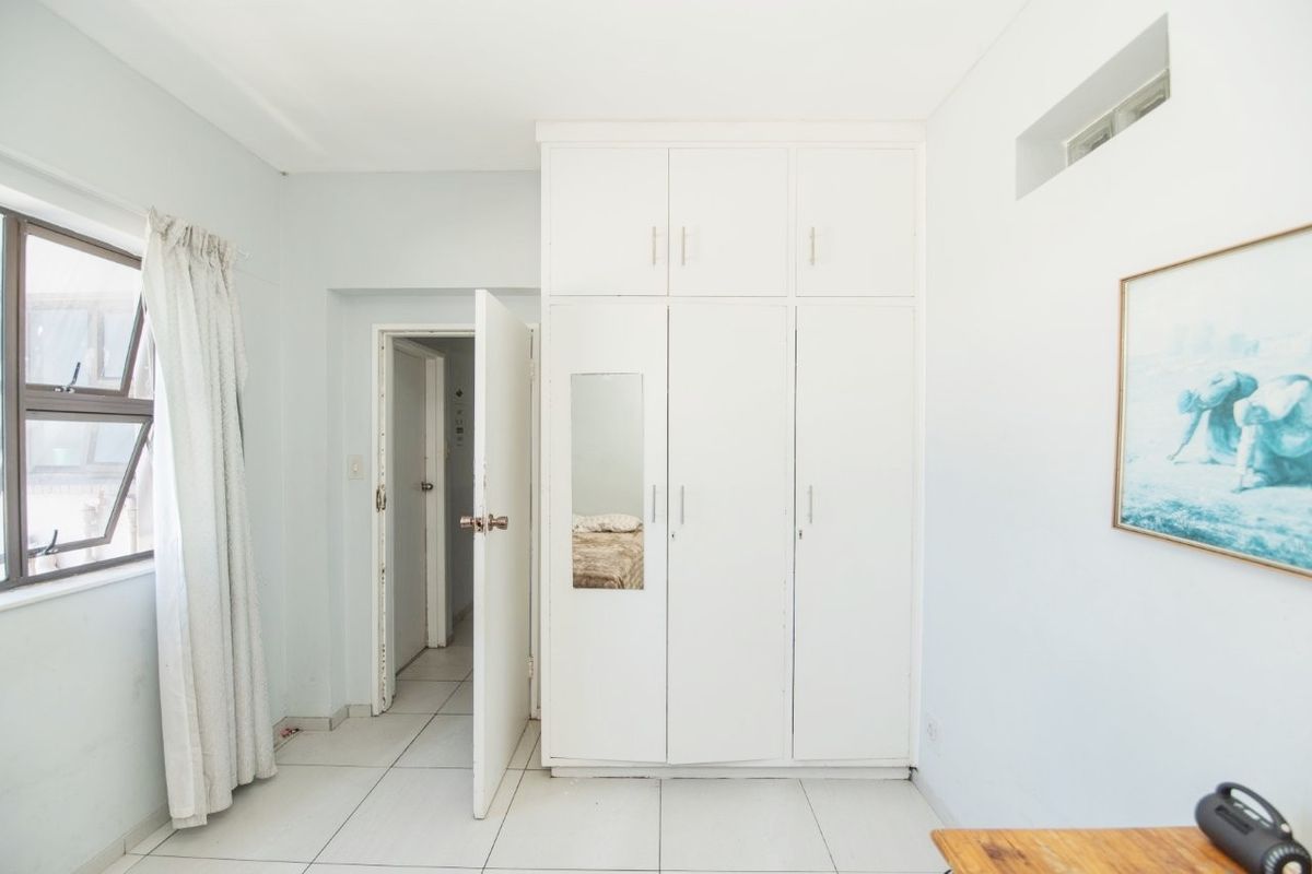 A bedroom featuring white built-in cupboards, tiled flooring, and natural light from an aluminium window.