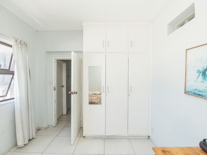 A bedroom featuring white built-in cupboards, tiled flooring, and natural light from an aluminium window.
