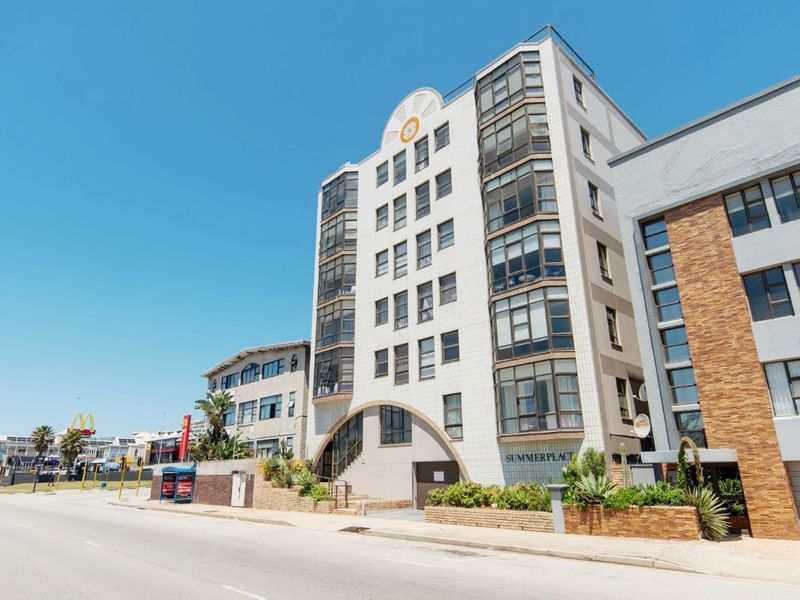 Street-level view of the Summerplace apartment building facade, featuring a multi-story structure with large windows and landscaped brick garden beds.