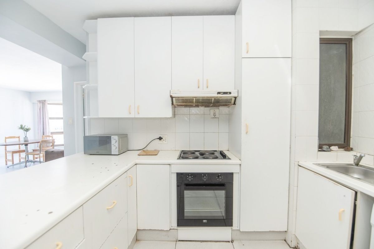 Compact kitchen featuring white cabinetry, built-in oven, electric hob, extractor fan, and a stainless steel sink with tiled backsplash.