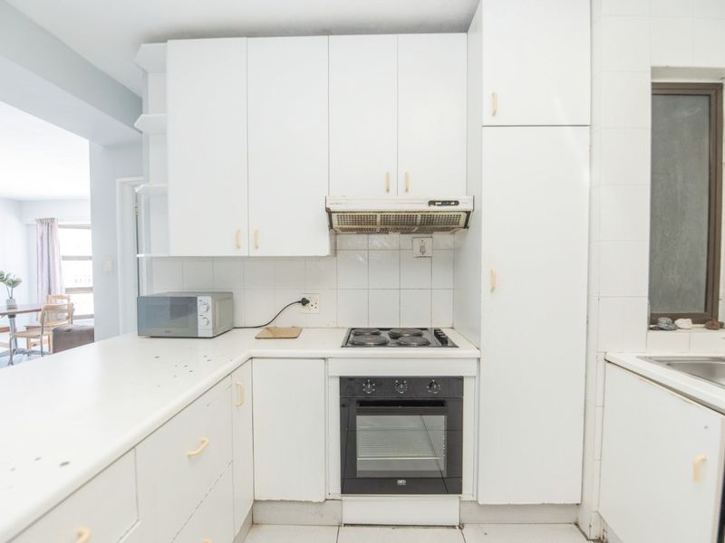 Compact kitchen featuring white cabinetry, built-in oven, electric hob, extractor fan, and a stainless steel sink with tiled backsplash.