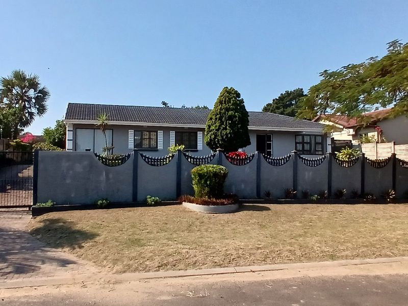 Front exterior view of a cottage featuring a paved driveway, secure perimeter wall with metal fencing, and a tiled roof.
