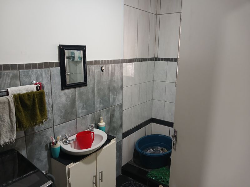 A functional bathroom featuring a vanity cabinet with a basin, wall tiling, and a dedicated shower area.