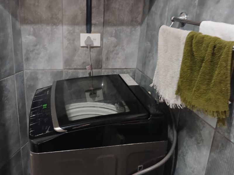 A functional laundry area featuring tiled walls, wall-mounted shelving, and dedicated plumbing connections for a washing machine.