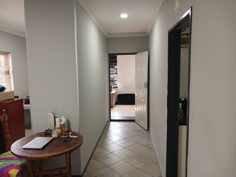 A clean, neutral-toned hallway featuring tiled flooring and recessed downlighting, providing access to adjacent rooms within the cottage.