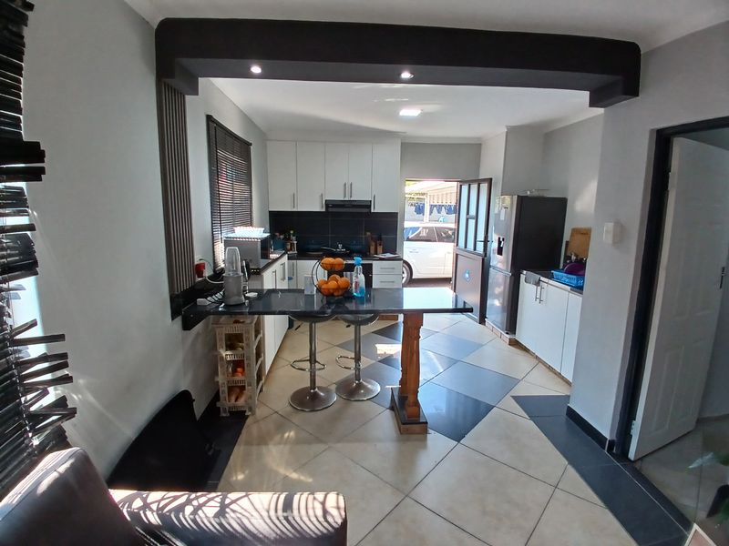 An open-plan kitchen area featuring modern white cabinetry, granite countertops, a breakfast bar, and tiled flooring with direct access to the exterior.