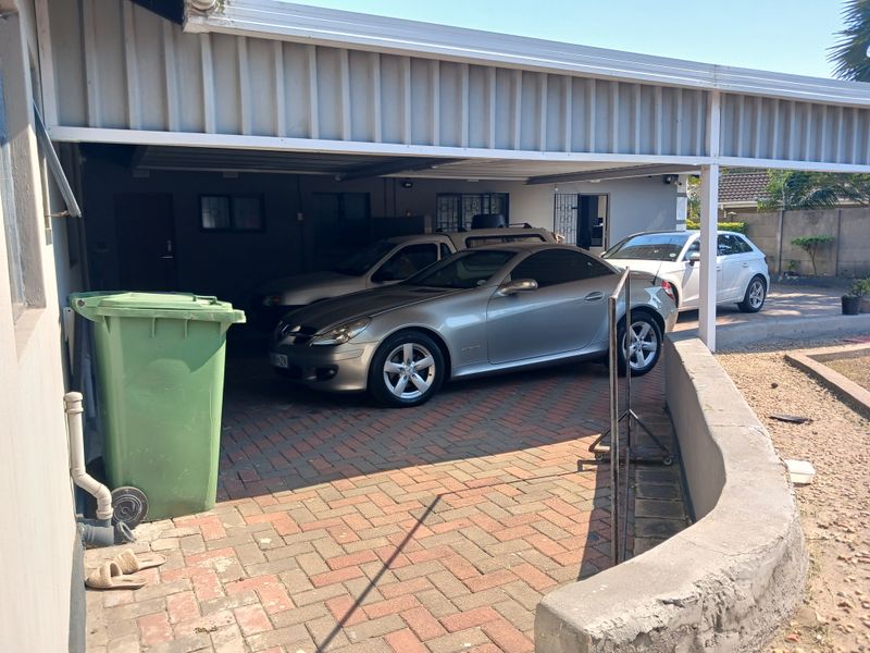 A covered carport area featuring paved flooring and a concrete retaining wall, providing sheltered off-street parking.