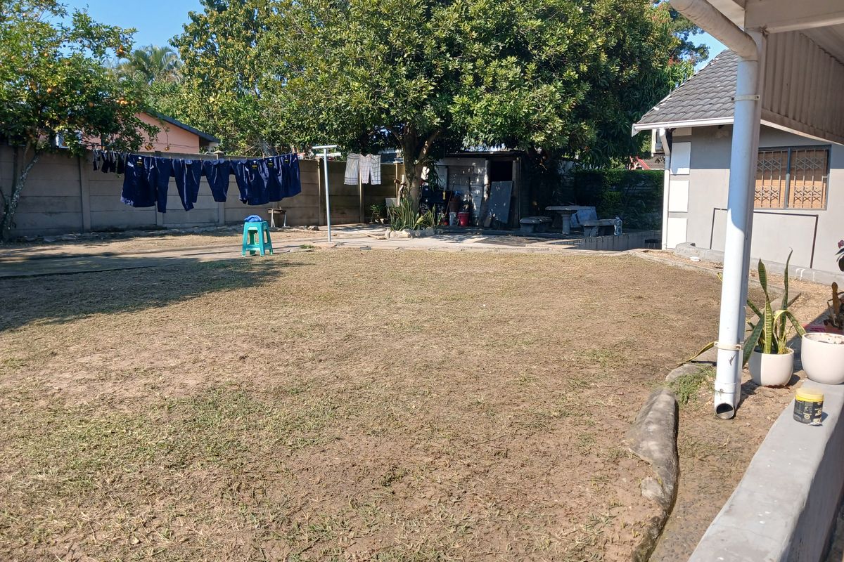 A spacious rear garden area featuring a large lawn, mature trees, and a precast concrete boundary wall, viewed from the side of the cottage.