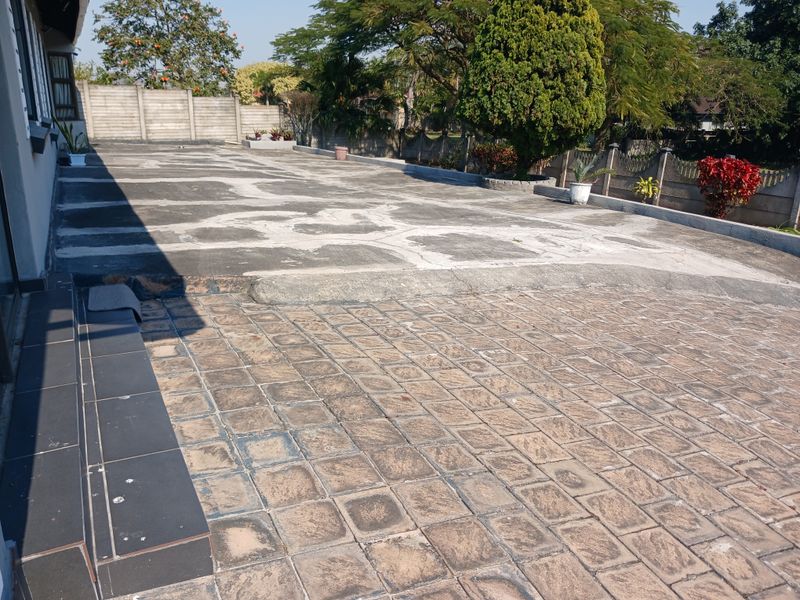 A spacious rear exterior area featuring a combination of paved surfaces and a concrete boundary wall, offering potential for landscaping or outdoor improvement.
