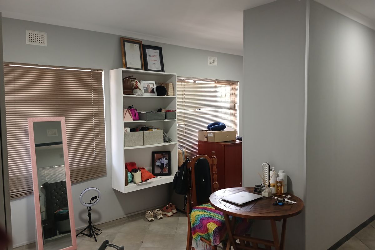 A living area featuring tiled flooring, neutral wall finishes, and venetian blinds, providing a functional space with built-in wall shelving.
