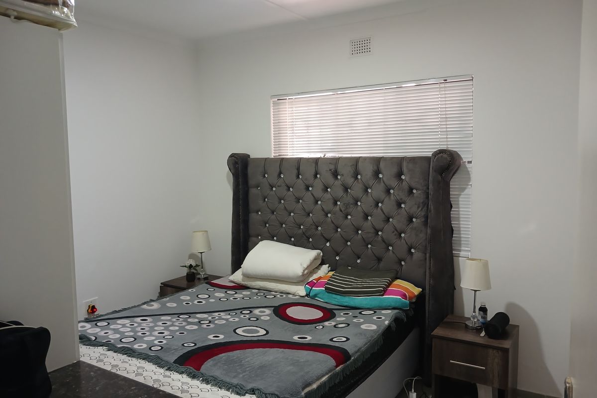 A bedroom featuring neutral walls, a ceiling vent, and venetian blinds covering the window.