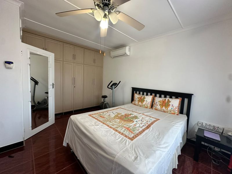 A bedroom featuring built-in cupboards, a ceiling fan, and a wall-mounted air conditioning unit with tiled flooring.