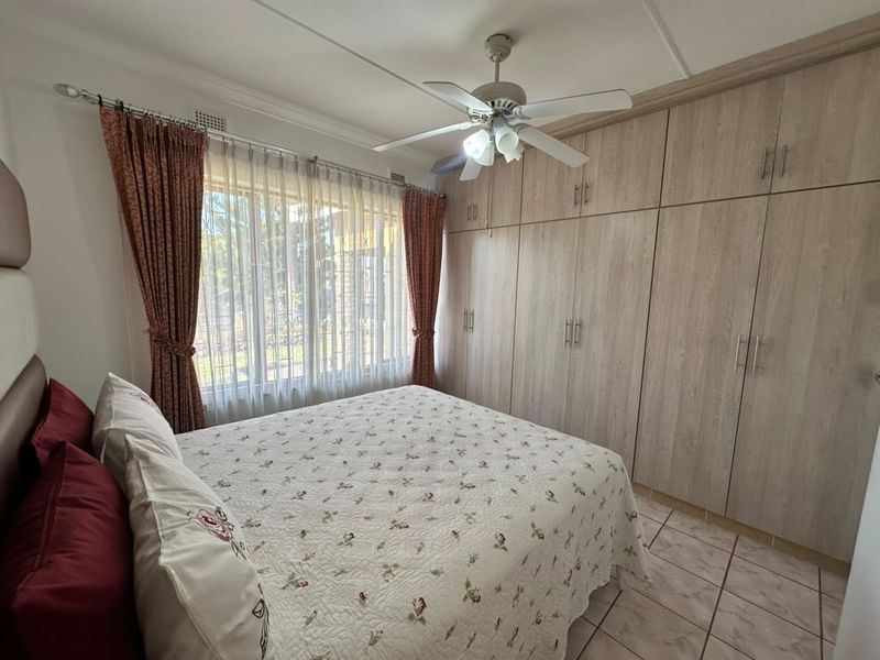 A well-maintained bedroom featuring extensive built-in wooden cupboards, a ceiling fan, and tiled flooring, offering ample storage and comfortable living space.