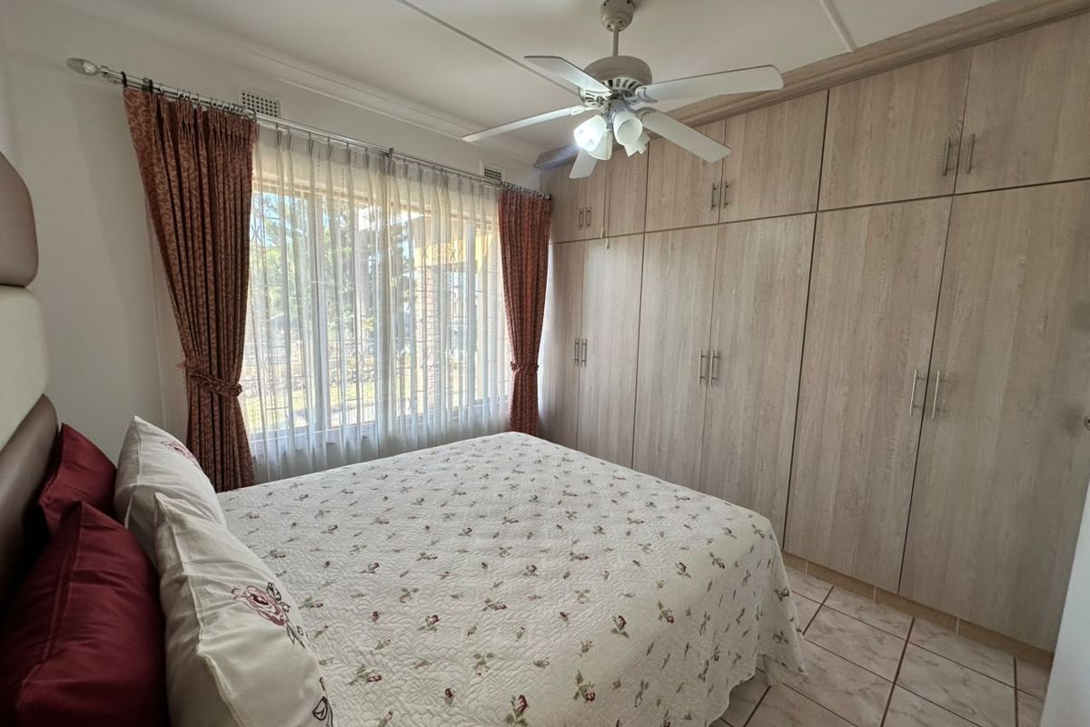 A well-maintained bedroom featuring extensive built-in wooden cupboards, a ceiling fan, and tiled flooring, offering ample storage and comfortable living space.