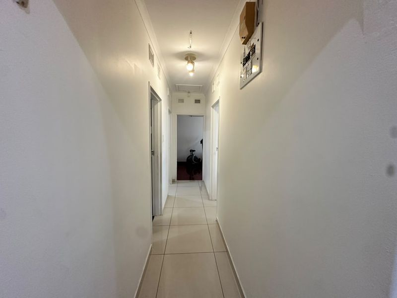 A clean, neutral hallway featuring tiled flooring, a ceiling light fixture, and a wall-mounted electrical distribution board.