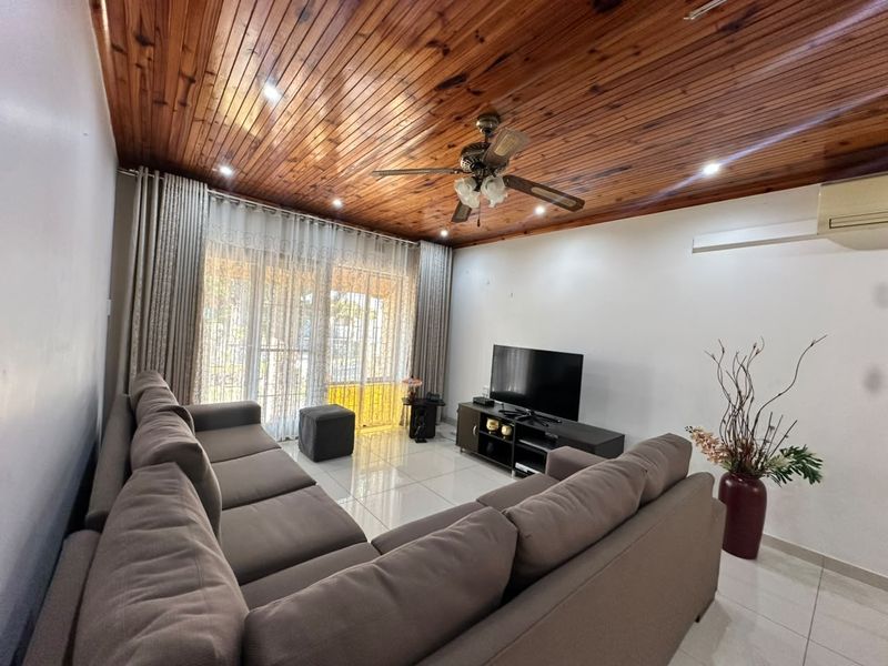 Spacious living room featuring a warm timber-paneled ceiling, tiled flooring, ceiling fan, and direct access to the outdoor area through sliding glass doors.