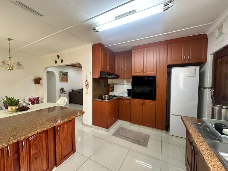 Open-plan kitchen featuring granite countertops, wooden cabinetry, built-in oven, and hob, seamlessly flowing into the adjacent dining and living areas.